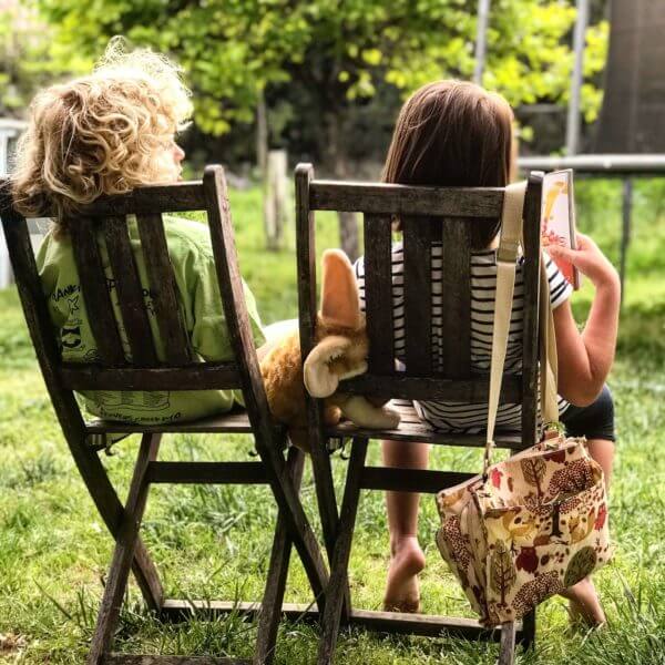 Two children sit on chairs in a garden. One reads a book. The ethics of smacking children are complex; consider the impact on kids' well-being.