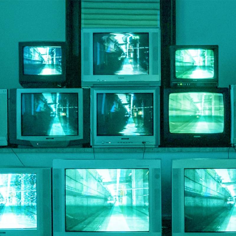 Media: Stack of old TVs displaying tunnels in shades of green and blue, creating an eerie, retro tech art installation.