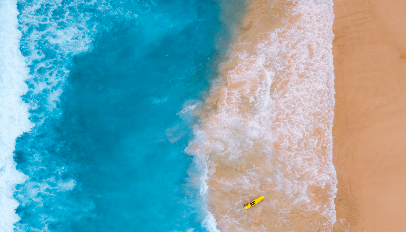 Aerial view of ocean waves meeting sandy beach with yellow surfboard. Beach scene with turquoise water.