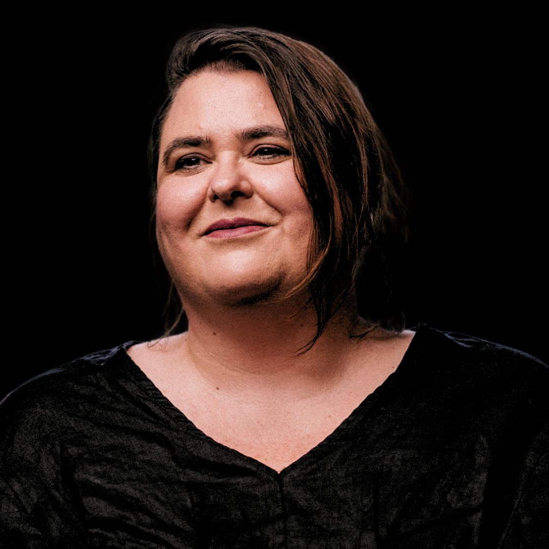 Danielle Harvey posing for a portrait in a dark studio setting wearing a textured black top with a soft and serene expression