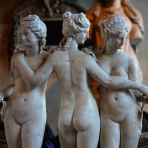 The Three Graces statue exemplifies classical beauty. Marble sculpture showing three nude women embracing, exploring ethics of beauty standards.