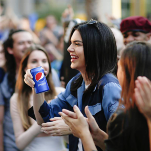 Kendall Jenner holds Pepsi can amid crowd, smiling. Corporate moral grandstanding, ethics of business, woke advertising controversy.