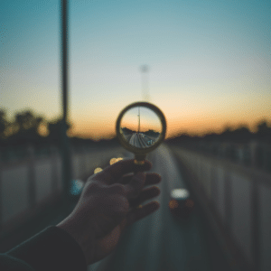 Teleology ethics explainer: Hand holding magnifying glass reflecting highway traffic at sunset, illustrating purpose and direction.
