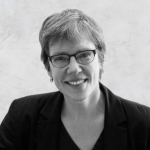 Black and white portrait of Sally Haslanger, a Big Thinker, wearing glasses and a blazer. She has short hair and a warm smile.