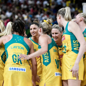 Australian netball team huddles in yellow and green uniforms with sponsor logos. Sponsorship dilemma: Is the money worth it for the team?