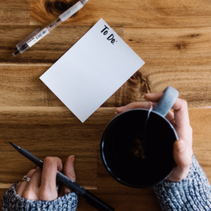 New Year's resolutions planning: hands holding tea, pens, and a To Do list on a wooden desk. Goal setting for the new year.