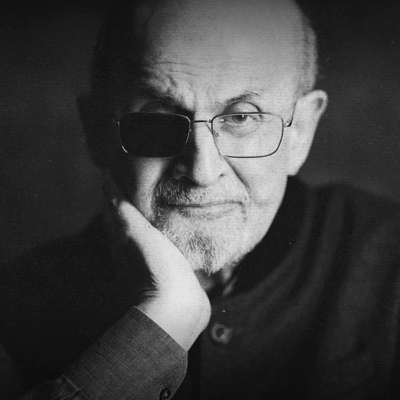 Media Releases: Black and white portrait of Salman Rushdie with glasses and a hand to his face. He has one eye covered.