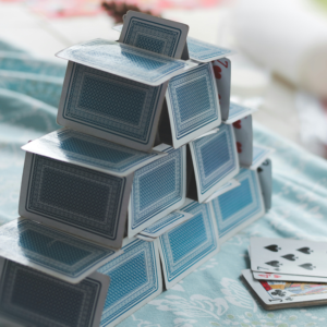 House of cards, a metaphor for ethical failure. Structure of playing cards on a patterned tablecloth, symbolizing fragility and risk.