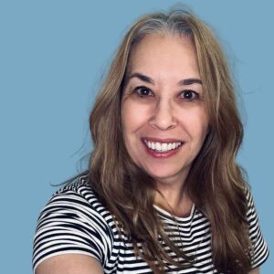 Lee-Anne Courtney's portrait. Smiling woman with long brown hair and a striped shirt against a blue background. Close-up headshot.