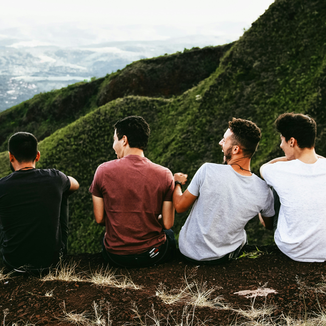 Four friends, seen from behind, sit on a hill overlooking a valley. The kind person isn't always the 'good guy'. Friendship concept.