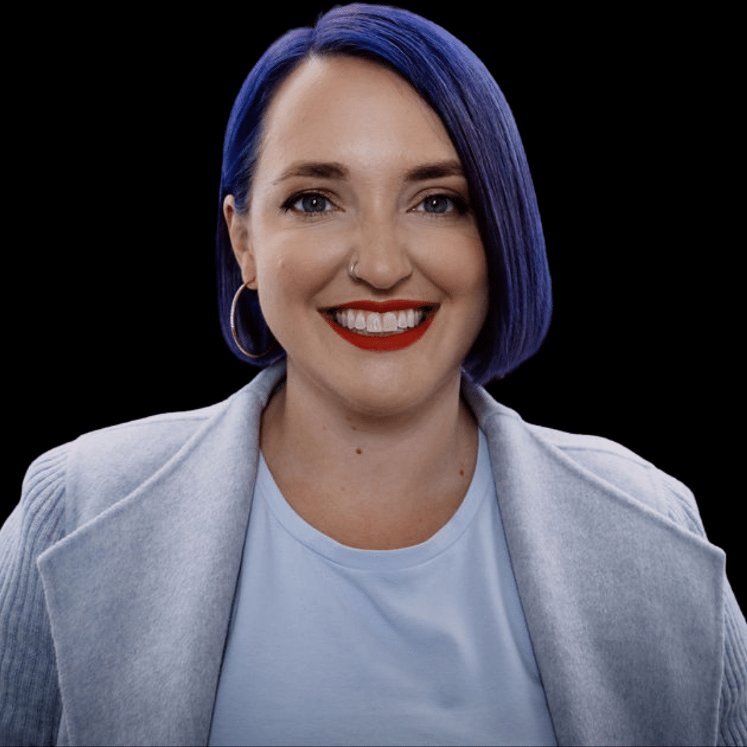 Aubrey Blanche's headshot. A smiling woman with short purple hair is set against a black backdrop. Professional portrait.
