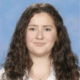 Headshot of Ariel Bai, a young woman with long, curly brown hair, fair skin, and a gentle smile, set against a blue background.
