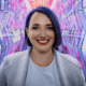 Aubrey Blanche, Director of responsible leadership, smiles with blue hair and red lipstick. A colorful geometric background is behind her.