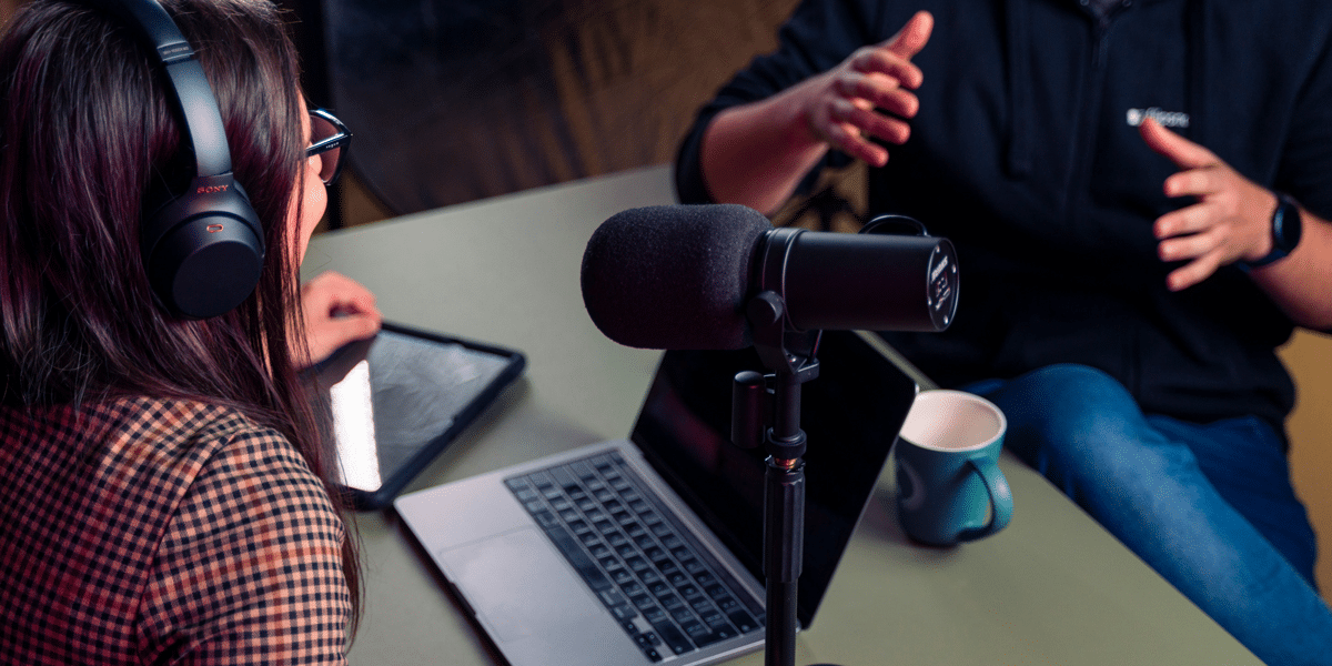 Media literacy podcast recording session. Woman with headphones, laptop, and microphone. Politics of platforming discussion.