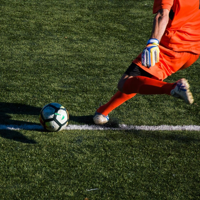 Soccer goalie in orange uniform kicking ball on green field. Free speech in sports, player action shot, competitive game.