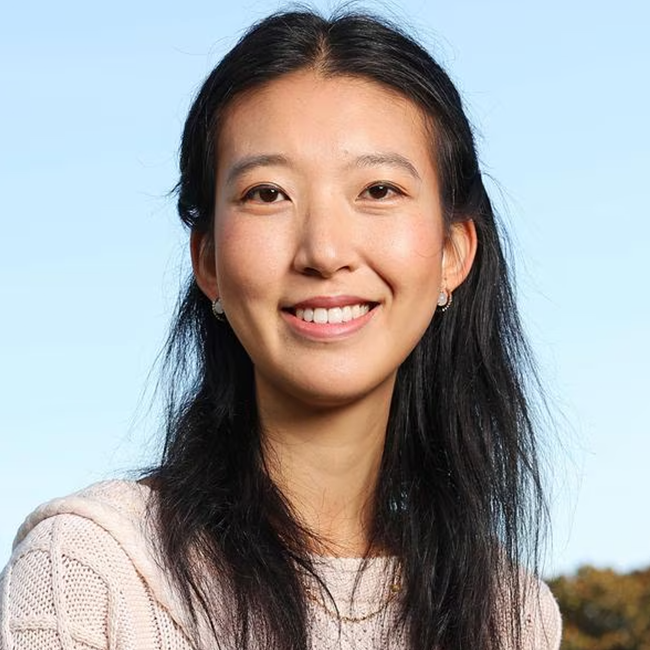 Portrait of a smiling Asian woman for The Ethics of Forgiveness. She has long black hair and is wearing a cream sweater. Sky background.