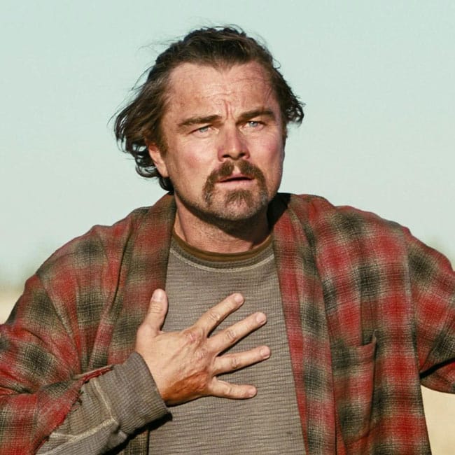 Leonardo DiCaprio portrays resistance in a scene from a political drama, wearing a plaid shirt and looking concerned, reflecting personal battles.