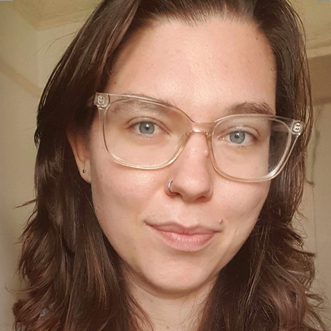 The Ethics of Bans: Close-up of a woman with glasses and a nose ring, light eyes, and brown hair, looking directly at the camera.