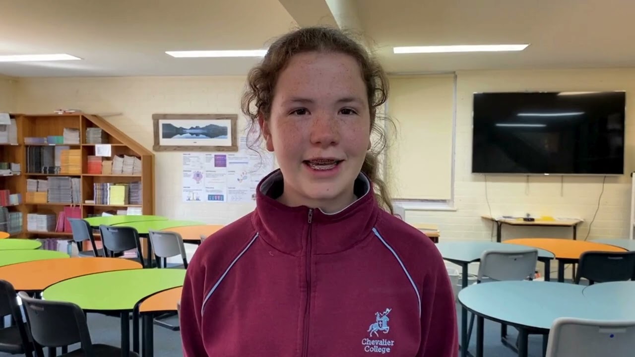 Student discusses racial discrimination video in classroom, wearing Chevalier College jacket, with desks and a TV visible behind her.