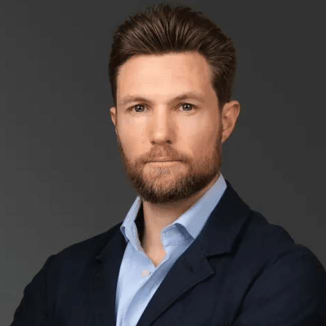 Richard Weir, an expert discussing the attention economy of suffering. Headshot of a man with beard in a blue shirt and navy jacket.