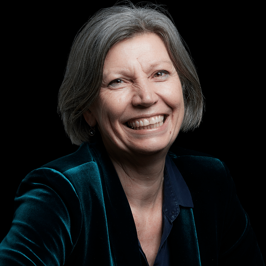 Governance expert with short grey hair, smiling broadly in a dark teal velvet blazer, promoting effective governance strategies and solutions.