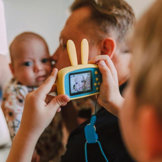 Child taking photo of baby with bunny-eared camera. Capturing playtime memories: The price of playtime is worth it for these adorable moments.
