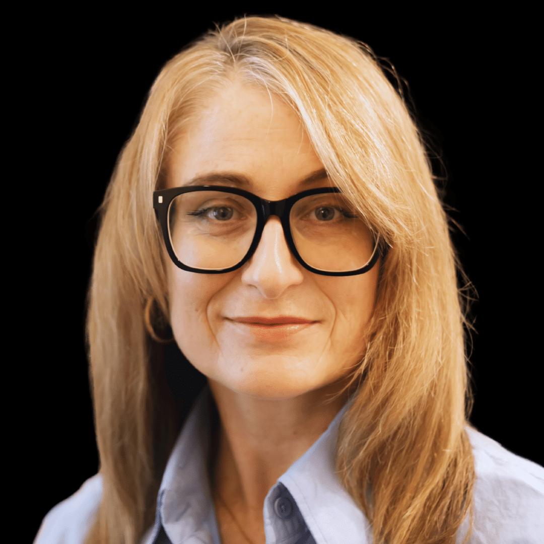Lauren Bennett portrait: Woman with blonde hair and black glasses, wearing a blue shirt against a black background. Professional headshot.