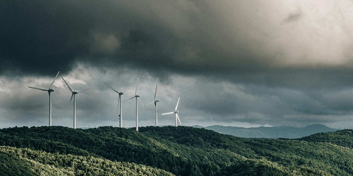 Wind turbines on a hill under a stormy sky. AI and risk concerns are visualized with renewable energy against a backdrop of uncertainty.