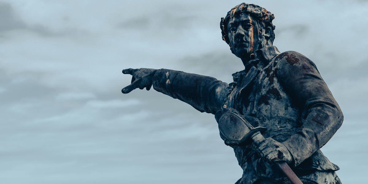 Close up of an aged stone sculpture showing a person gesturing towards the horizon under a muted and overcast morning sky