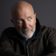 Richard Flanagan, author of Heresies, features in a thoughtful studio portrait with a shaved head and a grey trimmed beard