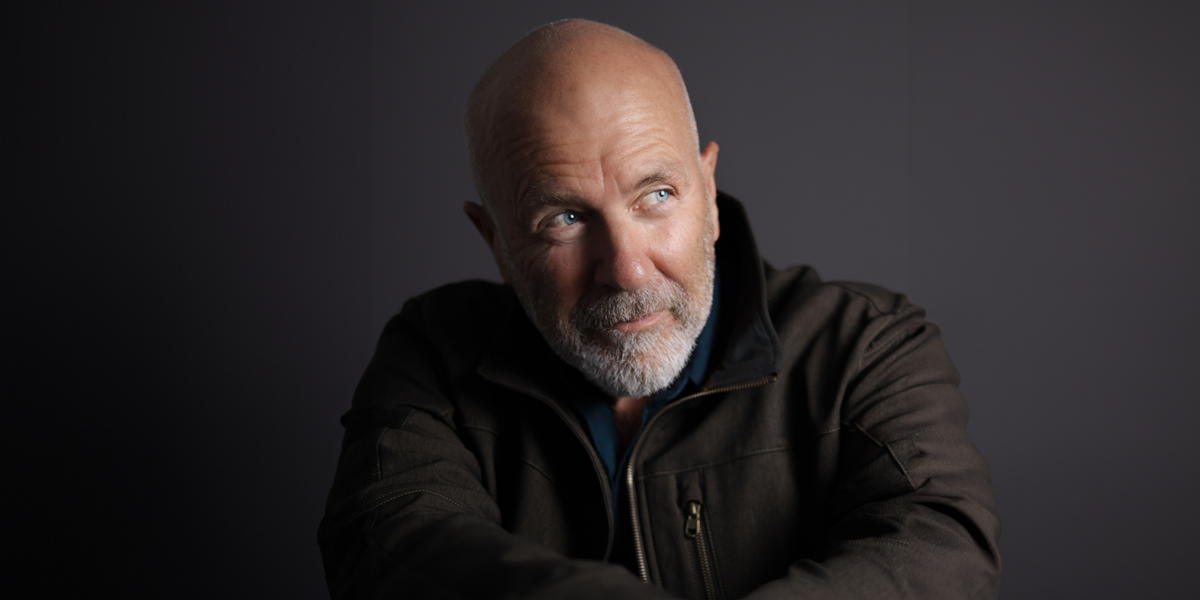 Writer Richard Flanagan gazes off-camera wearing a dark jacket in this dimly lit portrait for his book titled Heresies