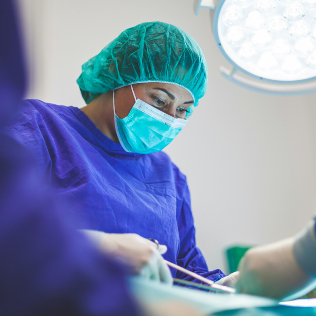 Female surgeon in blue scrubs and mask performing surgery under bright lights, representing medical care for prisoners.