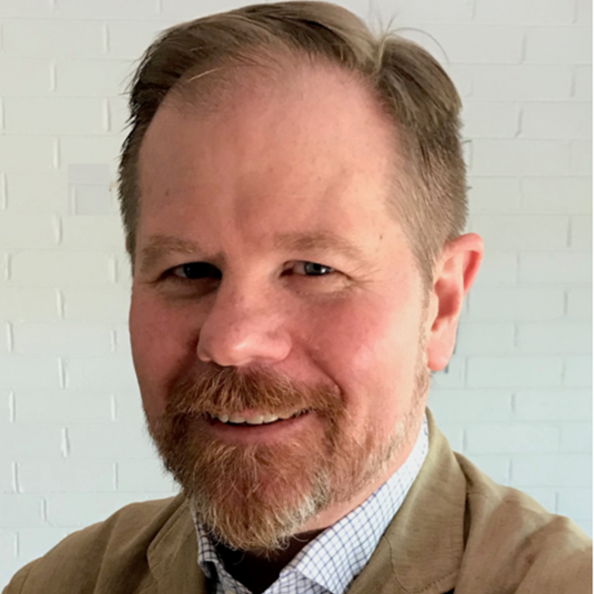 Portrait of a bearded man in a tan jacket and check shirt, relevant to the ethics of intervention discussion