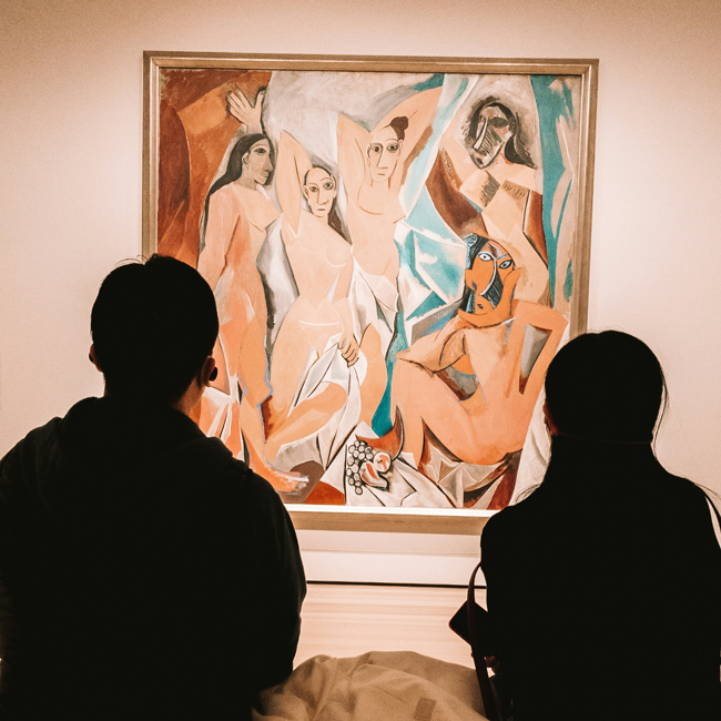 Two people standing in a gallery looking at the famous cubist painting Les Demoiselles d Avignon by the artist Pablo Picasso