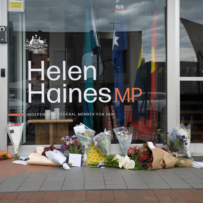 Helen Haines MP office window sign with flowers laid on pavement in tribute outside her electoral office