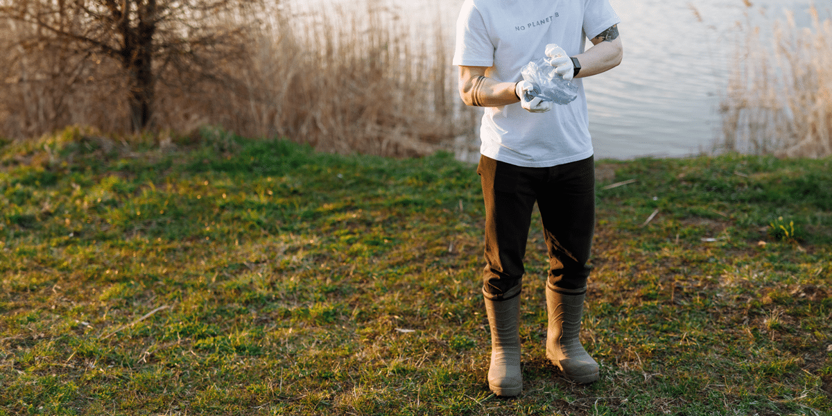 Tattooed arms in gloves clutching a bag, white shirt and tall boots, person standing in a grassy field doing the wrong thing