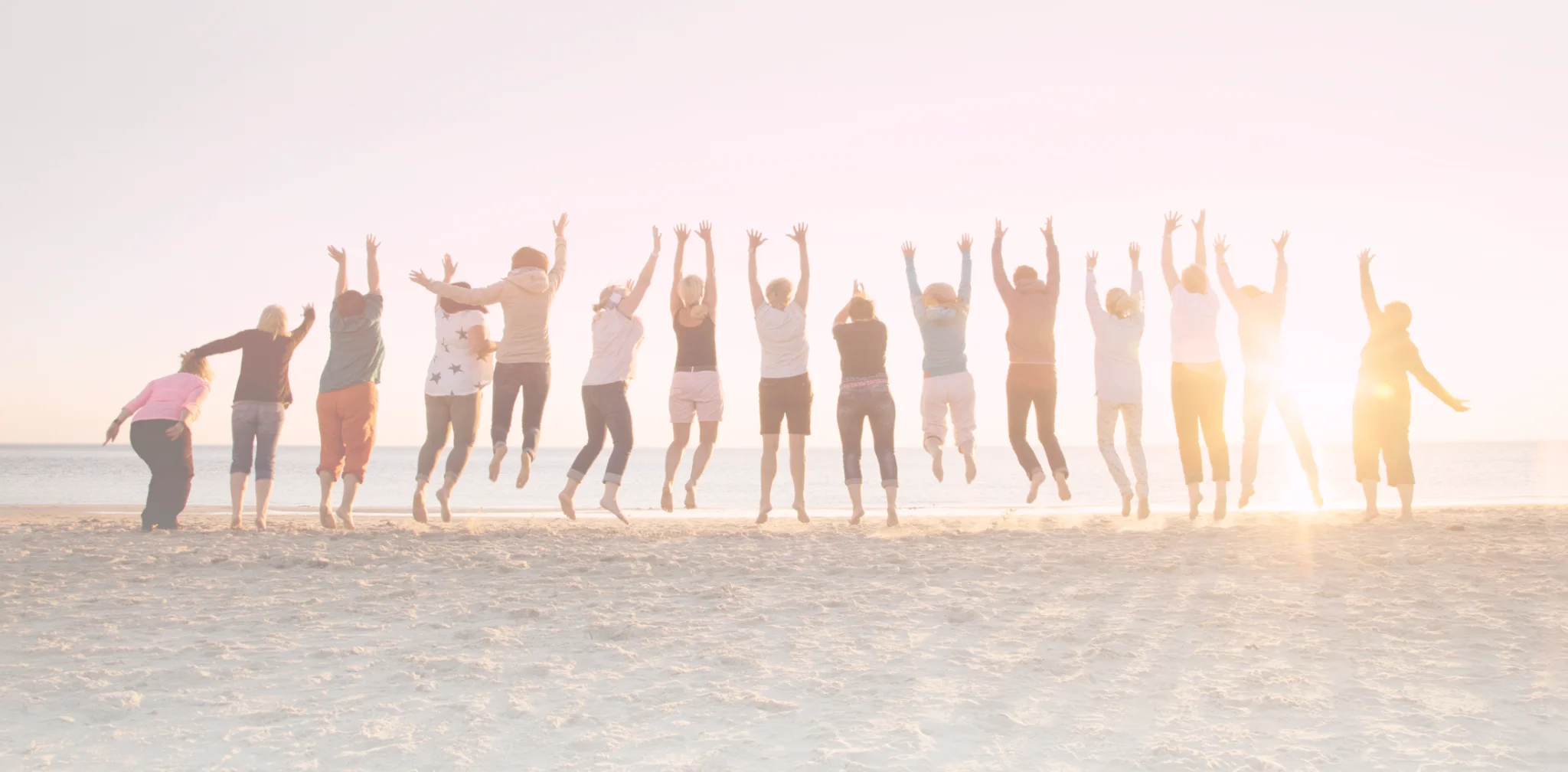 Group of people jumping on a beach at sunset, arms raised. Beachgoers celebrate with a jump, enjoying the sun and sand. Coastal fun and friendship.