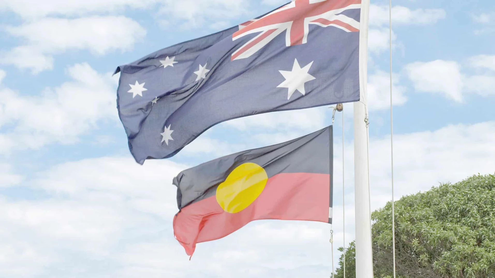 Australian and Aboriginal flags flying against a blue sky. The Australian flag is above the Aboriginal flag. The Aboriginal flag has a yellow circle.