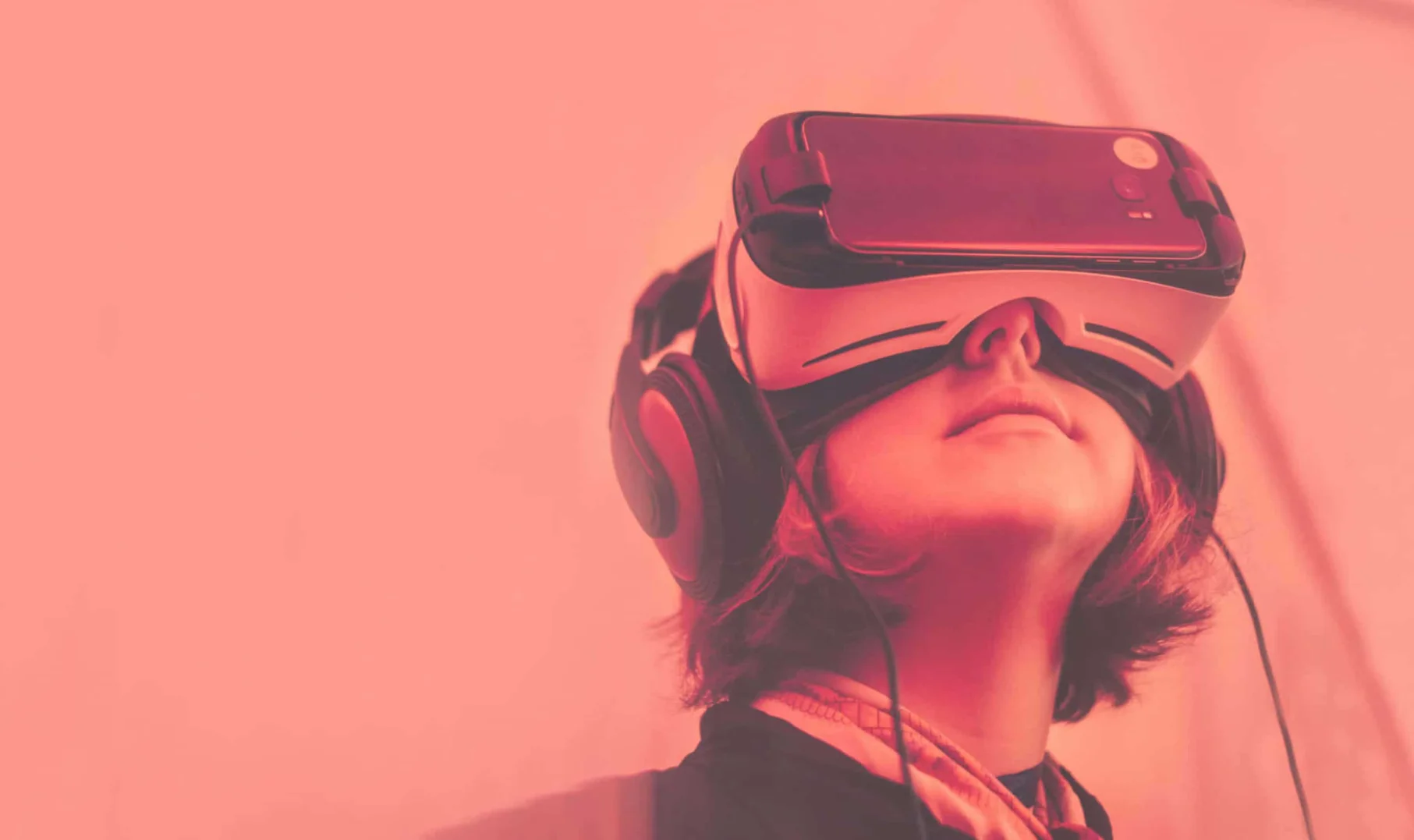 Media: Person wearing a VR headset and headphones, looking up. The background is a solid color. VR technology is immersive and engaging.
