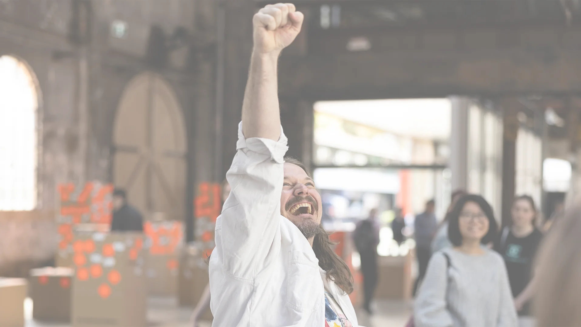 Enthusiastic man with raised fist in celebration. People and cardboard boxes with red dots are blurred in the background.